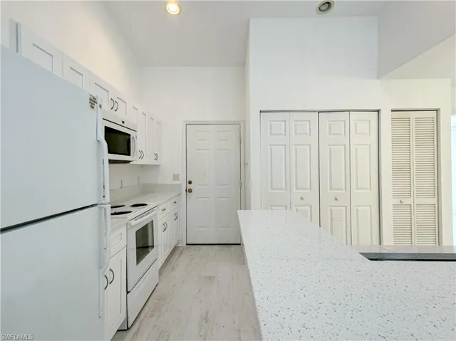 Kitchen featuring light stone counters, white appliances, light hardwood / wood-style floors, a towering ceiling, and white cabinetry