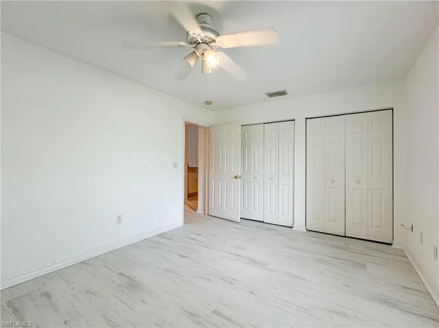 Unfurnished bedroom featuring light hardwood / wood-style flooring, ceiling fan, and multiple closets
