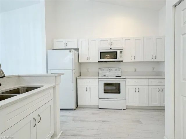 Kitchen with sink, light wood-type flooring, white appliances, white cabinets, and lofted ceiling