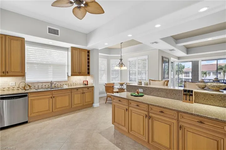 Kitchen with light stone counters, backsplash, stainless steel dishwasher, recessed lighting, and brown cabinets