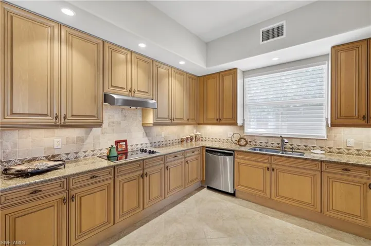 Kitchen with recessed lighting, light stone countertops, decorative backsplash, stainless steel dishwasher, and brown cabinetry