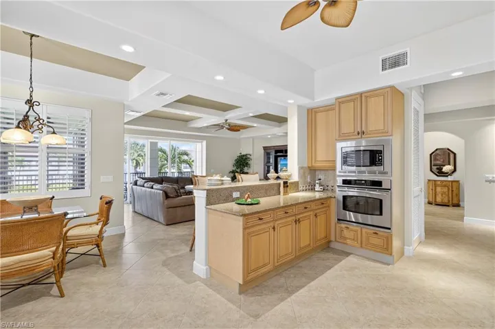 Kitchen featuring coffered ceiling, open floor plan, a ceiling fan, light stone counters, and appliances with stainless steel finishes