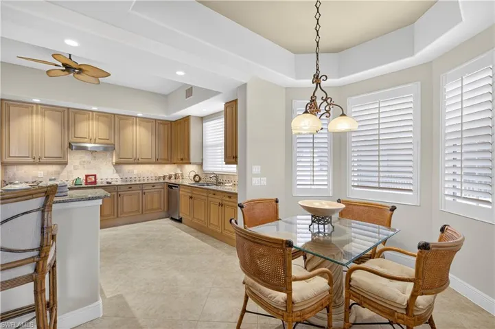 Kitchen with dark stone counters, a tray ceiling, tasteful backsplash, hanging light fixtures, and brown cabinets