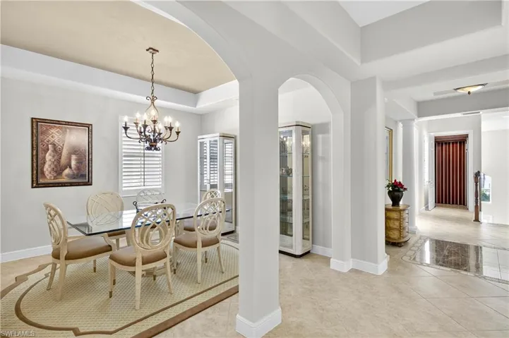 Dining area featuring arched walkways, light tile patterned floors, a raised ceiling, and a chandelier