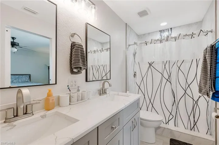 Full bathroom with double vanity, toilet, ensuite bathroom, a shower with curtain, and a ceiling fan