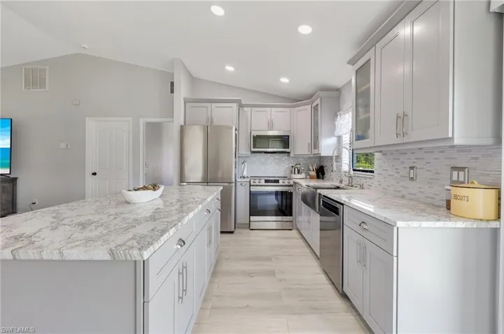 Kitchen featuring appliances with stainless steel finishes, vaulted ceiling, tasteful backsplash, a kitchen island, and glass insert cabinets