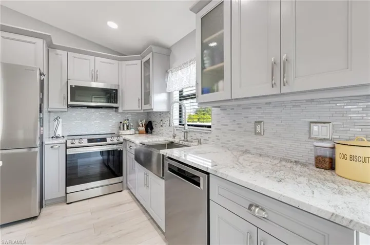 Kitchen featuring stainless steel appliances, a sink, vaulted ceiling, backsplash, and light stone countertops