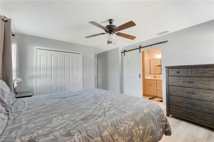 Bedroom with a barn door, a closet, a sink, ceiling fan, and light wood-type flooring