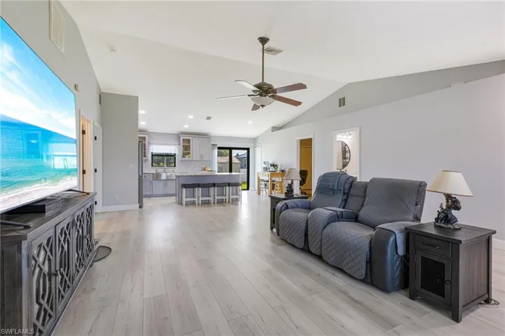 Living area with vaulted ceiling, a ceiling fan, and light wood-type flooring