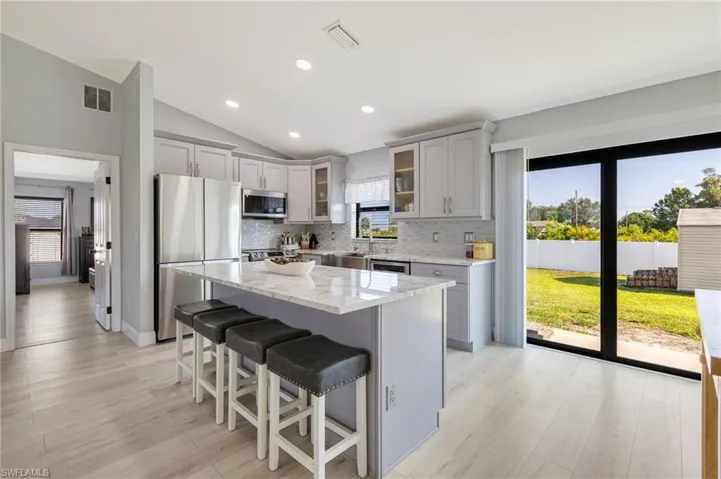 Kitchen featuring appliances with stainless steel finishes, gray cabinetry, tasteful backsplash, a kitchen breakfast bar, and vaulted ceiling
