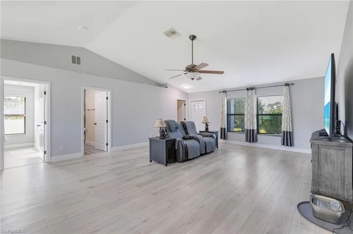 Living room with a ceiling fan, lofted ceiling, light wood-style flooring, and baseboards