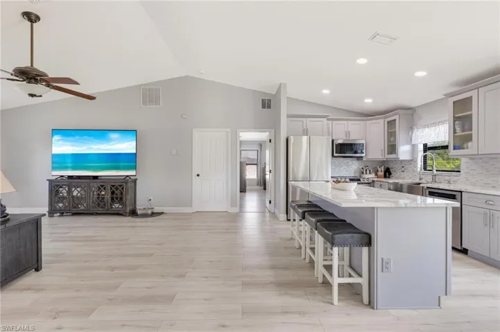 Kitchen featuring stainless steel appliances, open floor plan, a kitchen island, a ceiling fan, and light stone countertops