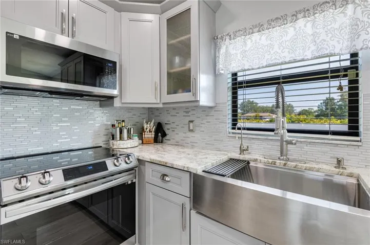 Kitchen with appliances with stainless steel finishes, a sink, tasteful backsplash, and glass insert cabinets