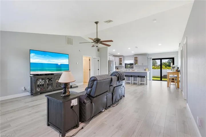 Living area featuring vaulted ceiling, light wood-style floors, ceiling fan, and baseboards