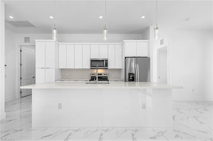 Kitchen with white cabinets, stainless steel appliances, tasteful backsplash, light marble finish flooring, and hanging light fixtures
