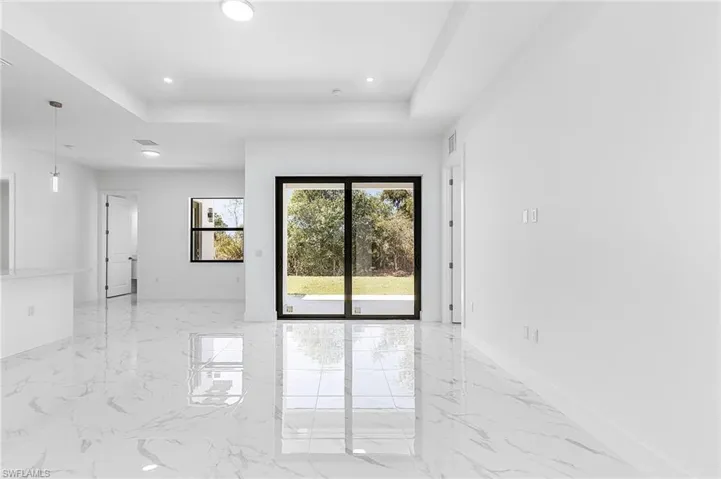 Empty room featuring a raised ceiling, light marble finish flooring, and recessed lighting