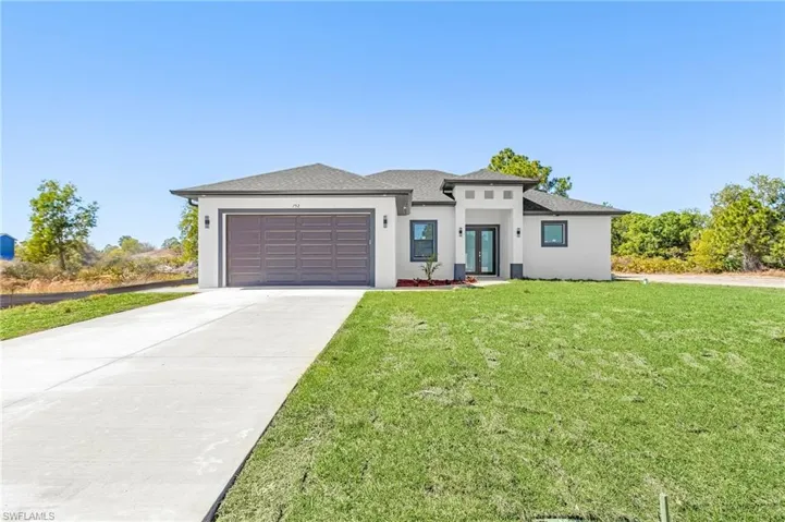 Prairie-style home featuring concrete driveway, an attached garage, stucco siding, a front lawn, and roof with shingles
