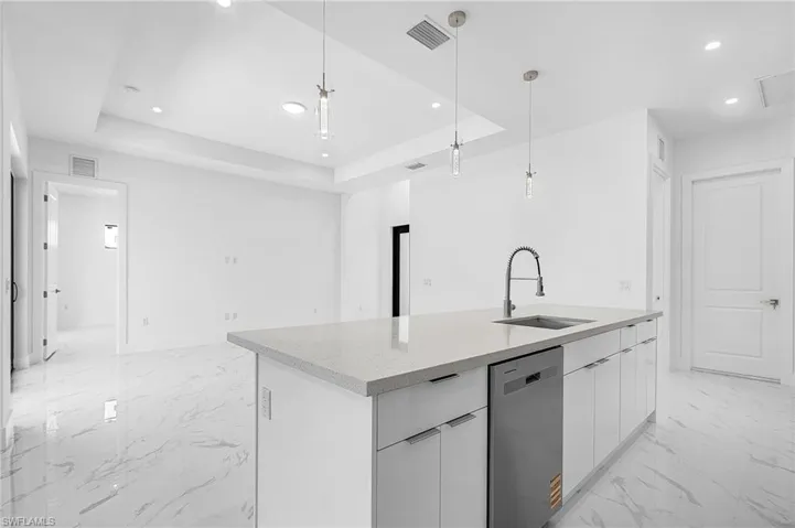 Kitchen with modern cabinets, pendant lighting, a tray ceiling, stainless steel dishwasher, and white cabinetry