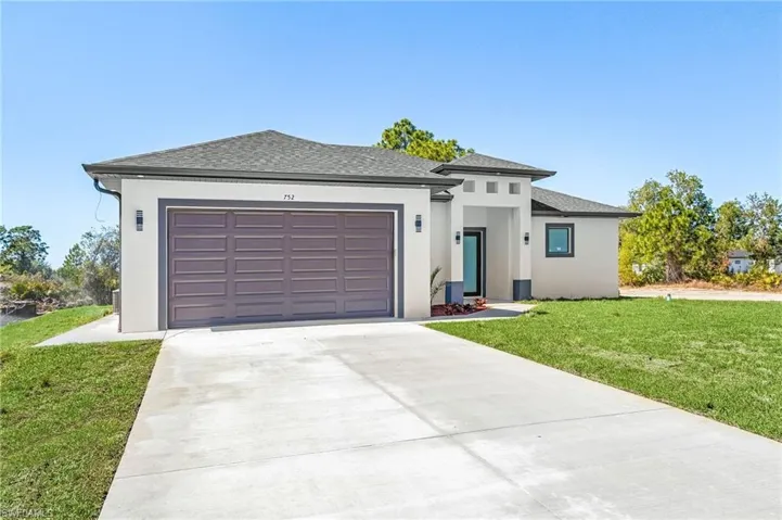 Prairie-style home featuring a front lawn, a shingled roof, concrete driveway, stucco siding, and an attached garage