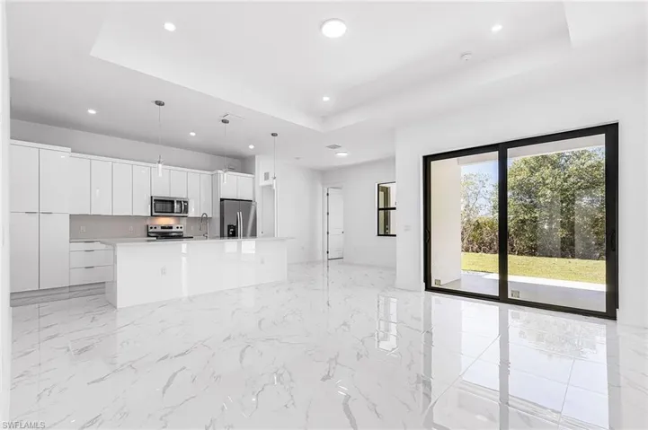 Kitchen with white cabinetry, a tray ceiling, pendant lighting, stainless steel appliances, and a kitchen island with sink