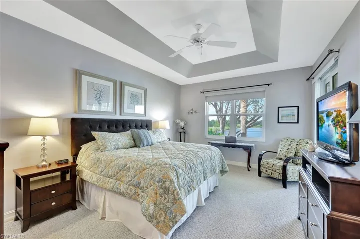 Carpeted bedroom featuring ceiling fan and a tray ceiling