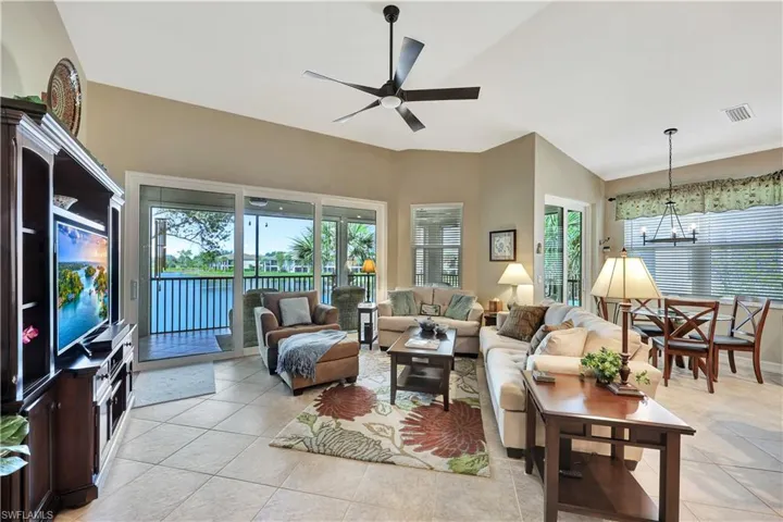 Living room featuring lofted ceiling, ceiling fan with notable chandelier, light tile patterned floors, and a wealth of natural light