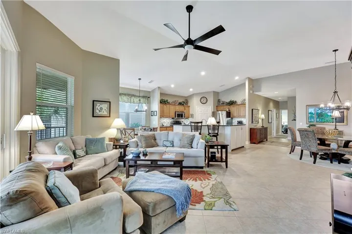 Tiled living room featuring ceiling fan with notable chandelier and vaulted ceiling