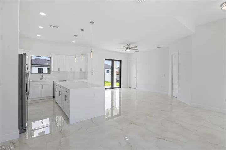 Kitchen with tasteful backsplash, a kitchen island, light tile floors, hanging light fixtures, and white cabinets