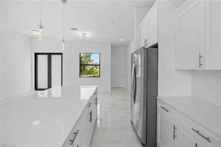 Kitchen featuring light stone countertops, decorative light fixtures, light tile flooring, white cabinets, and stainless steel refrigerator