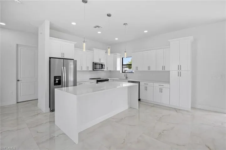 Kitchen with decorative light fixtures, a kitchen island, light tile floors, white cabinets, and appliances with stainless steel finishes