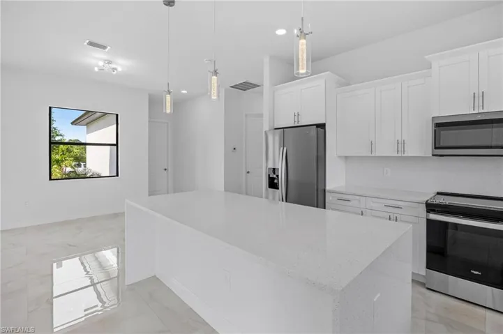 Kitchen with appliances with stainless steel finishes, white cabinetry, hanging light fixtures, and light tile flooring