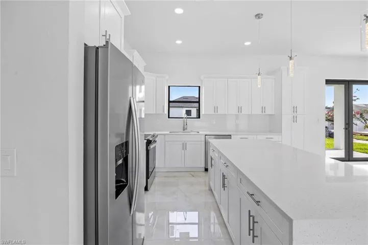 Kitchen with stainless steel appliances, white cabinets, light tile floors, and pendant lighting