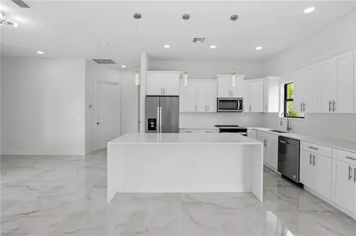 Kitchen featuring decorative light fixtures, backsplash, a center island, white cabinetry, and appliances with stainless steel finishes