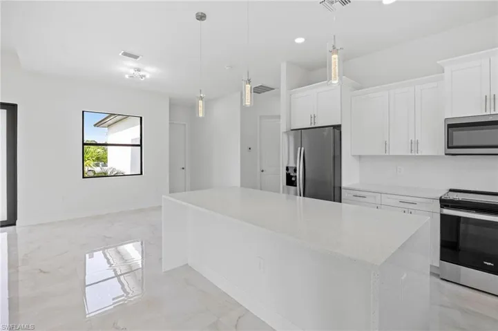 Kitchen featuring a center island, white cabinets, light tile flooring, and appliances with stainless steel finishes