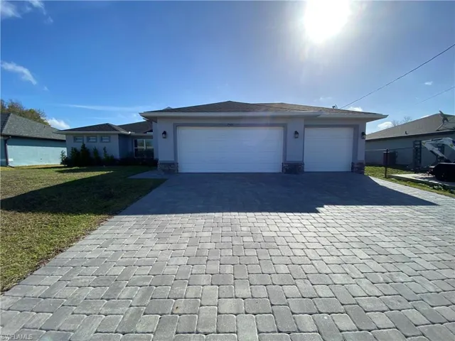 Ranch-style house with stone siding, decorative driveway, a front lawn, a garage, and stucco siding
