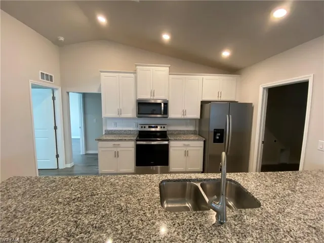 Kitchen with stainless steel appliances, recessed lighting, white cabinetry, light stone counters, and vaulted ceiling