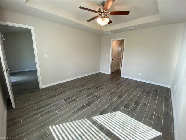 Empty room with a raised ceiling, wood finish floors, and ceiling fan