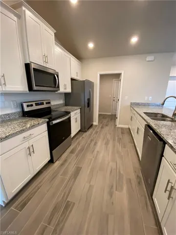 Kitchen featuring white cabinetry, stainless steel appliances, light stone counters, dark wood-style floors, and recessed lighting