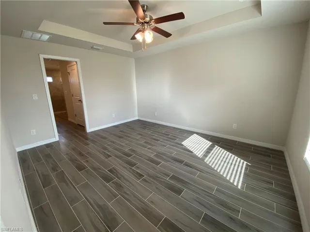 Unfurnished room featuring a raised ceiling, wood tiled floors, and ceiling fan