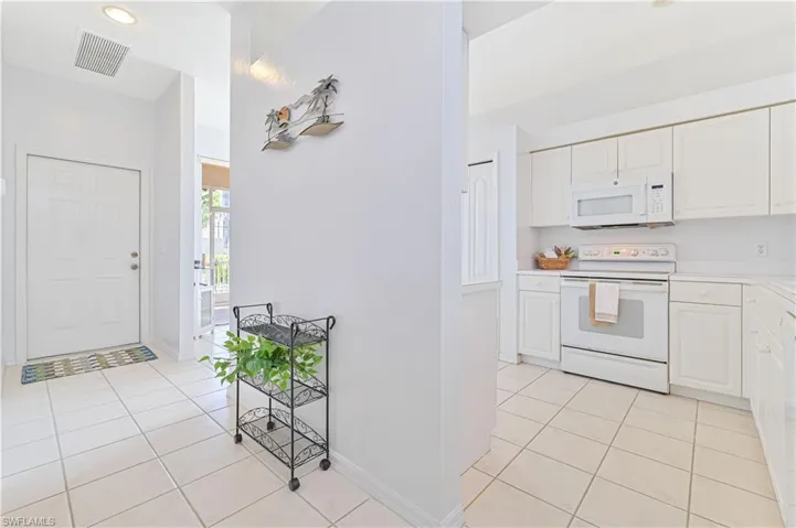 Kitchen with white appliances, light tile patterned floors, light countertops, and white cabinets
