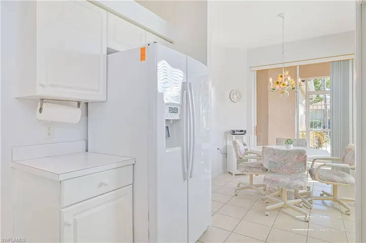 Kitchen featuring white refrigerator with ice dispenser, white cabinets, light countertops, a chandelier, and light tile patterned flooring