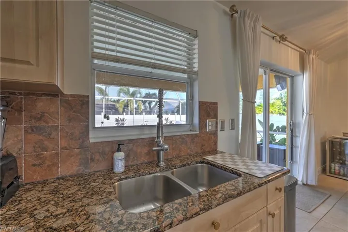 Kitchen featuring light brown cabinets, dark stone countertops, light tile patterned floors, and plenty of natural light