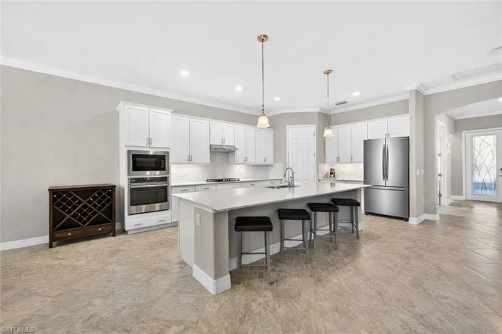 Kitchen featuring arched walkways, stainless steel appliances, ornamental molding, white cabinetry, and a spacious island
