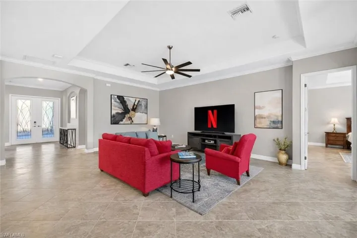 Living room featuring arched walkways, french doors, a raised ceiling, crown molding, and a ceiling fan