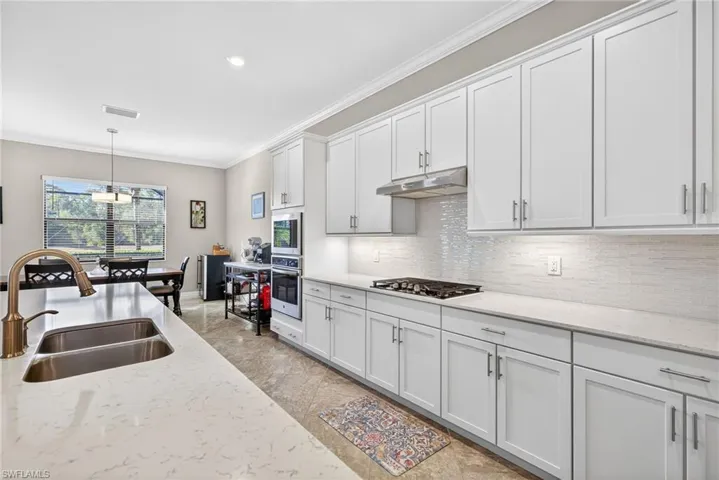 Kitchen with hanging light fixtures, light stone counters, white cabinetry, crown molding, and stainless steel appliances