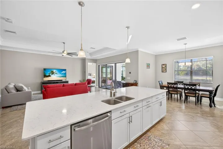 Kitchen with white cabinets, dishwasher, light stone countertops, pendant lighting, and a center island with sink