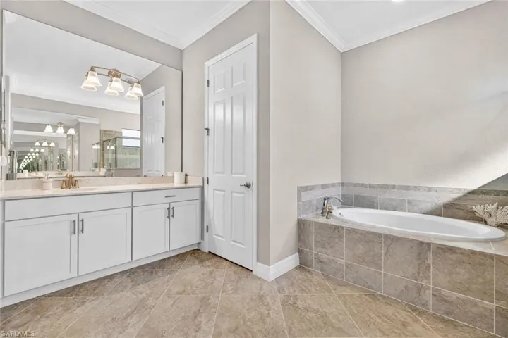 Full bath featuring vanity, ornamental molding, a garden tub, and an enclosed shower