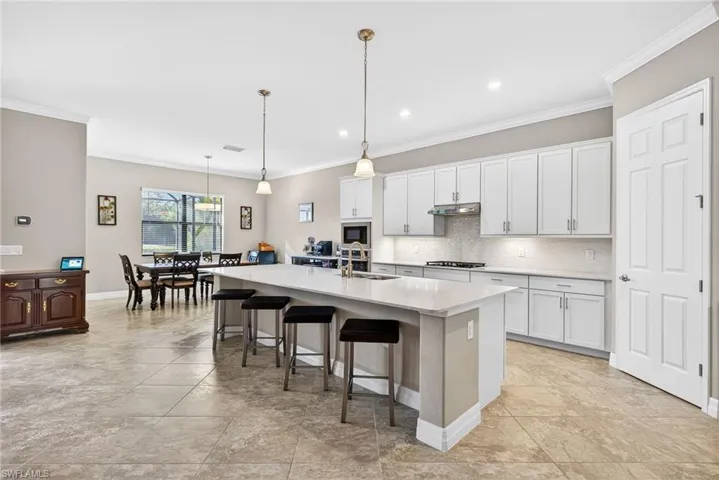 Kitchen featuring a kitchen bar, a center island with sink, hanging light fixtures, white cabinetry, and ornamental molding