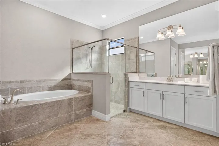 Full bath featuring vanity, a stall shower, ornamental molding, and a garden tub