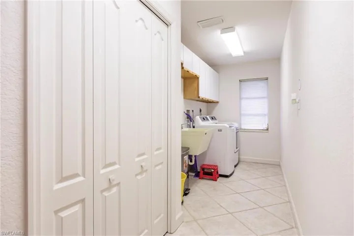 Clothes washing area featuring cabinets, light tile floors, and washing machine and clothes dryer